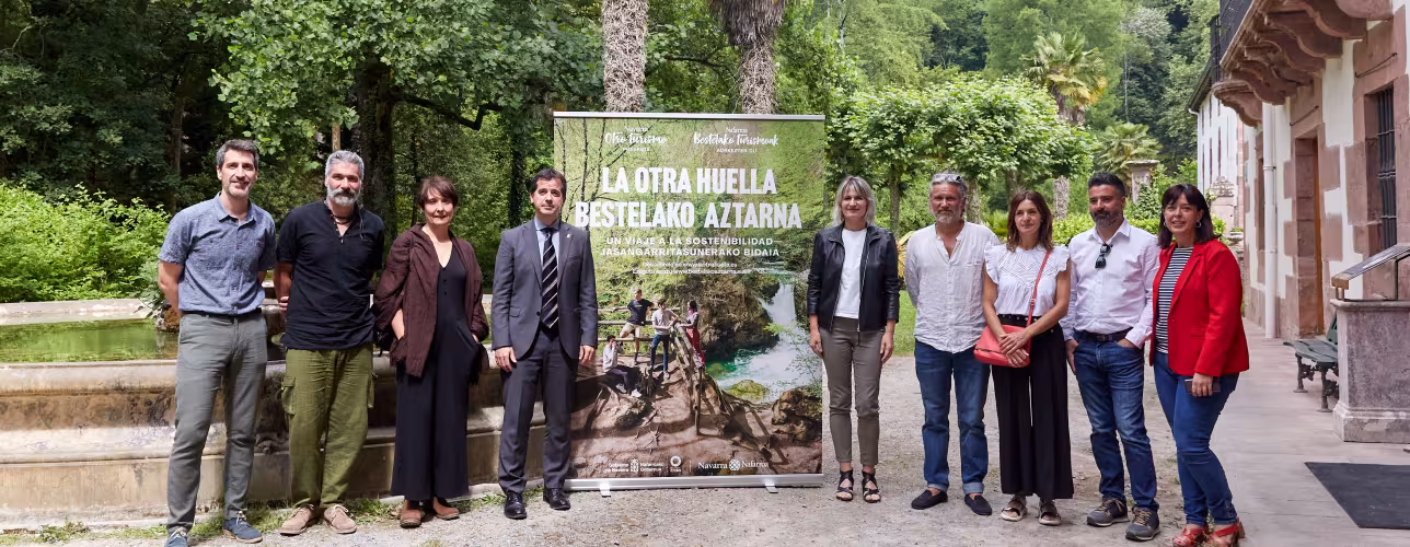 El consejero Irujo, la directora general Maitena Ezkutari, otras y otros representantes del Gobierno de Navarra, Nasertic, de la agencia de creatividad Hermosa y de Blua Producciones posan con el cartel que presenta el documental "La Otra Huella" de Turismo.