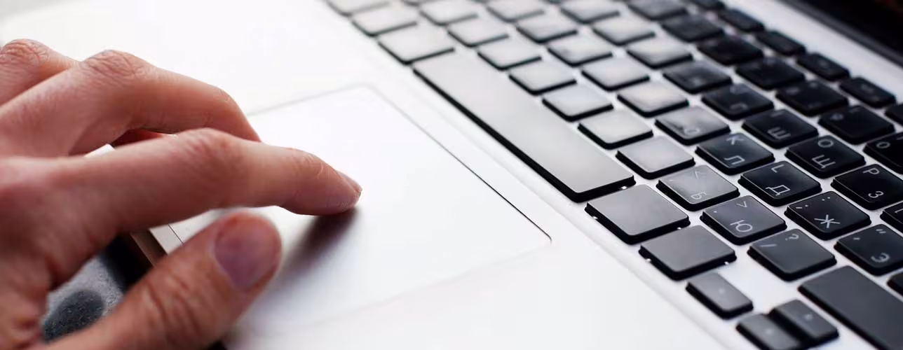 Mano utilizando el panel táctil (trackpad) de un ordenador portátil con teclado visible en primer plano.